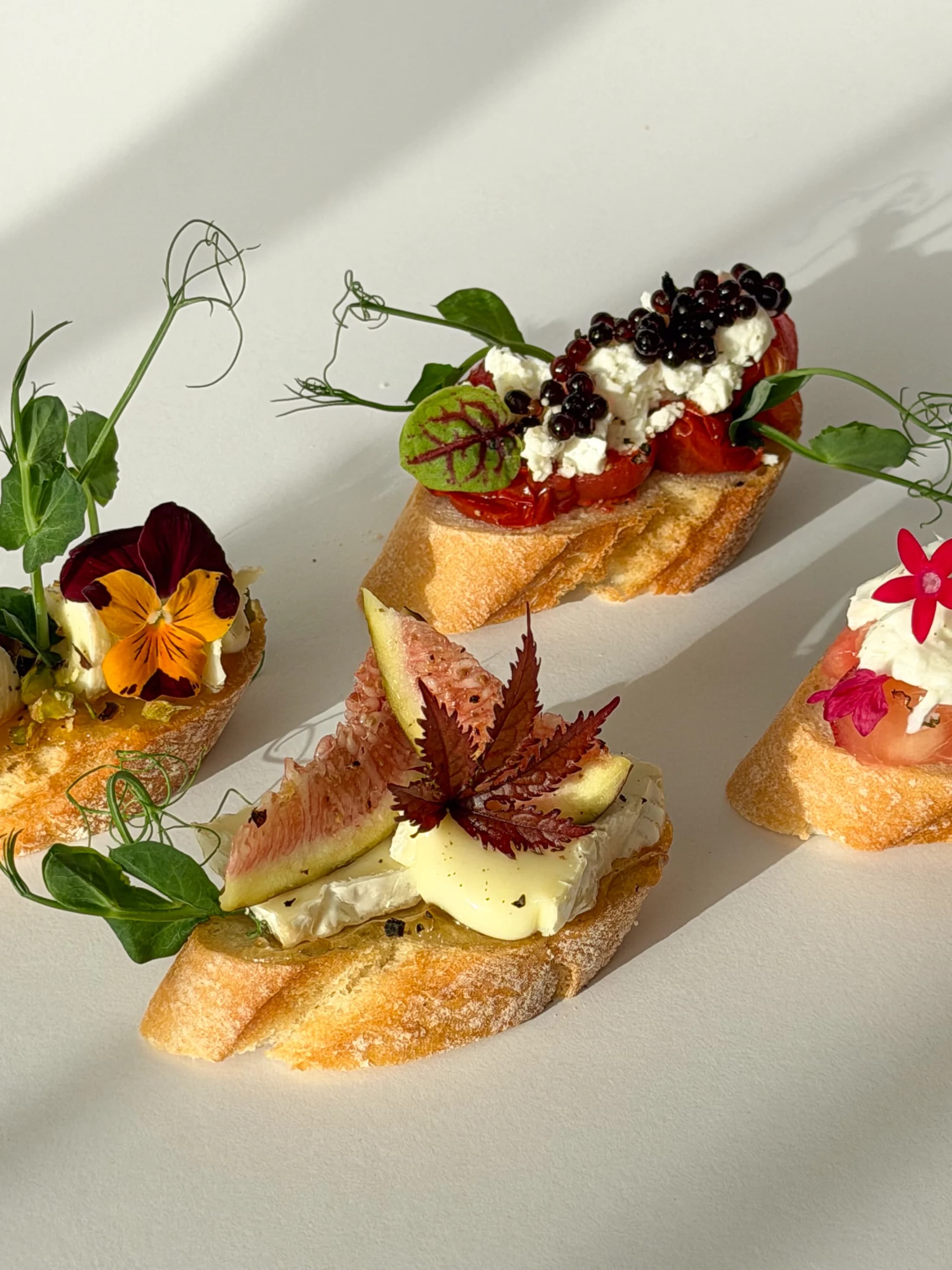 Cheese and fig canapes with edible flowers and herbs on a cream tabletop.